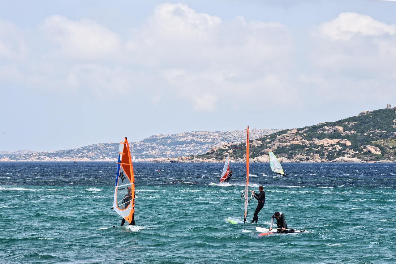 Spiaggia siciliana ideale per sport acquatici, con praticanti di windsurf e kite che cavalcano le onde.
