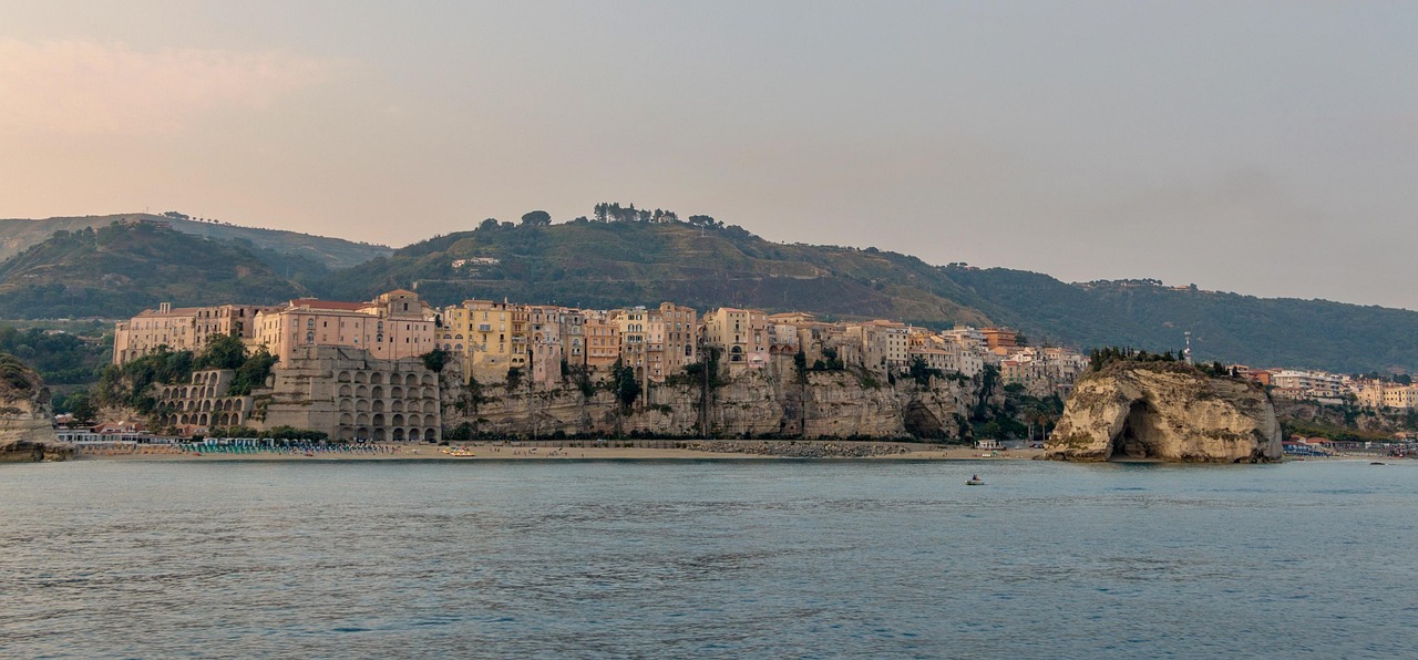 Vista panoramica della costa siciliana al tramonto, con colori caldi e silhouette di scogliere.