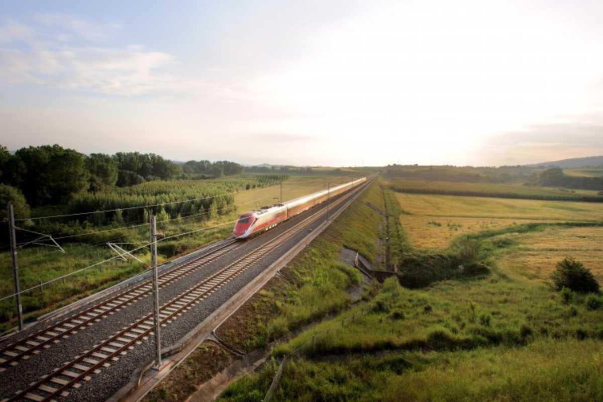 Treno veloce a due piani in partenza per Parigi, con passeggeri a bordo e paesaggio italiano sullo sfondo.